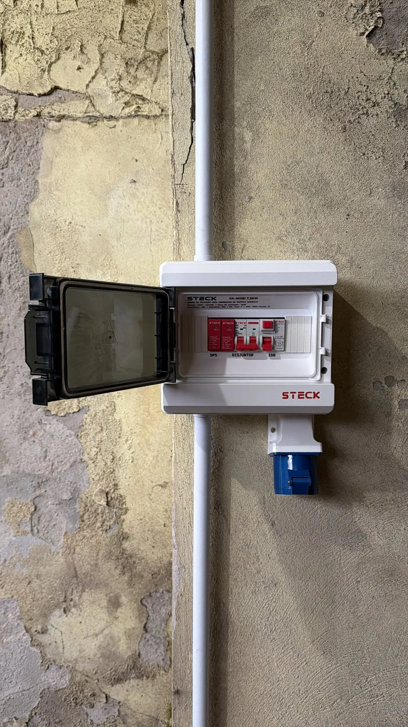 Quadro de proteção instalado em parede de concreto com tomada industrial azul abaixo